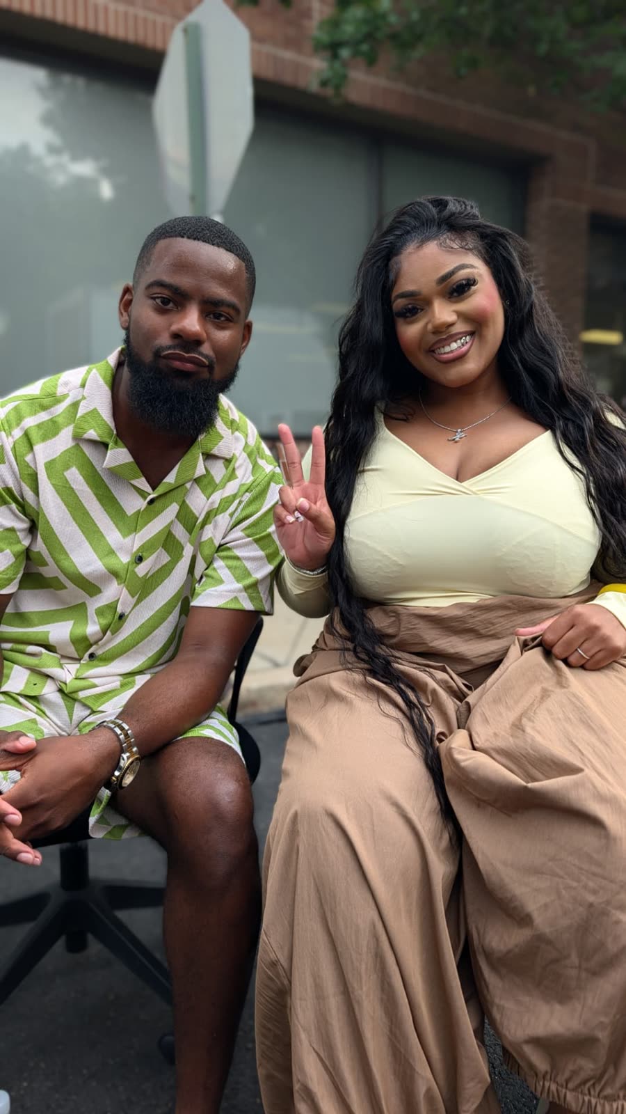Nasir Leach seated outdoors beside a smiling guest flashing a peace sign